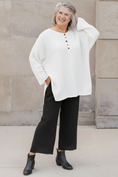 Woman wearing an orange top and black pants standing against a stone wall.